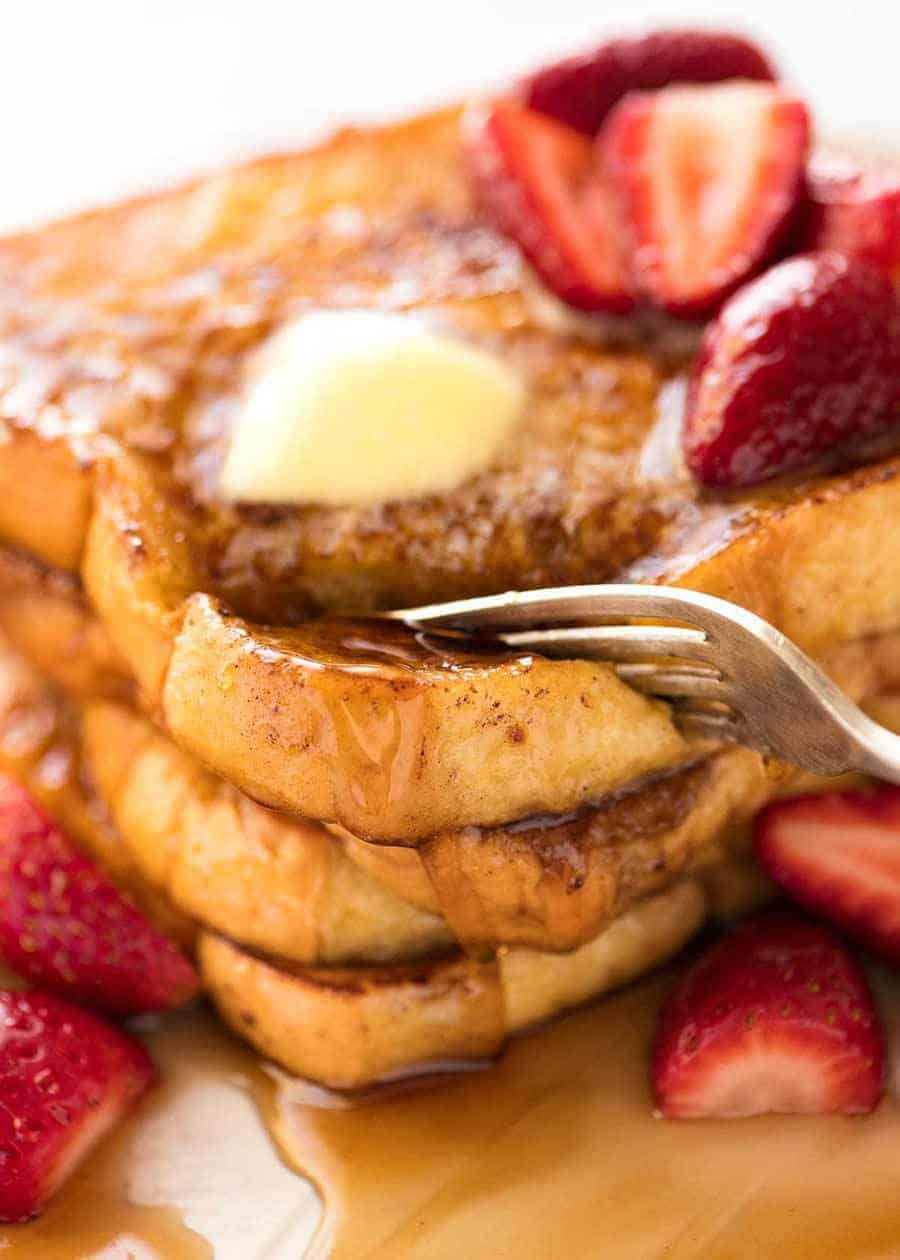 Fork cutting into a stack of French Toast smothered in maple syrup