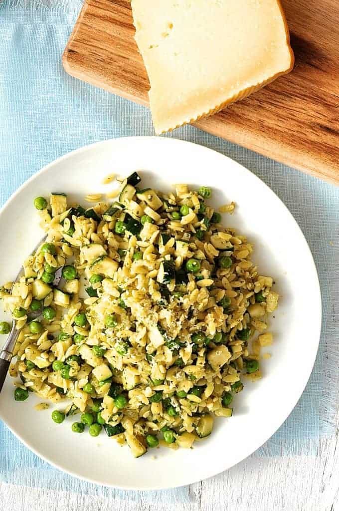 Pea, Zucchini and Pesto Orzo / Risoni on a white plate with parmesan on the side.