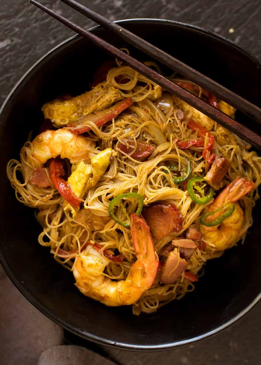 Overhead photo of Singapore Noodles in a black bowl with chopsticks resting on the edge, ready to be eaten.