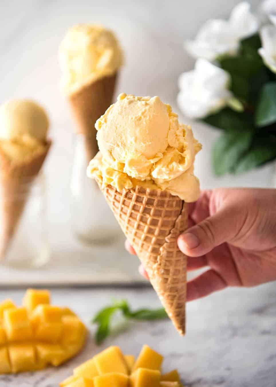 Ice cream cone with mango ice cream held in a hand.