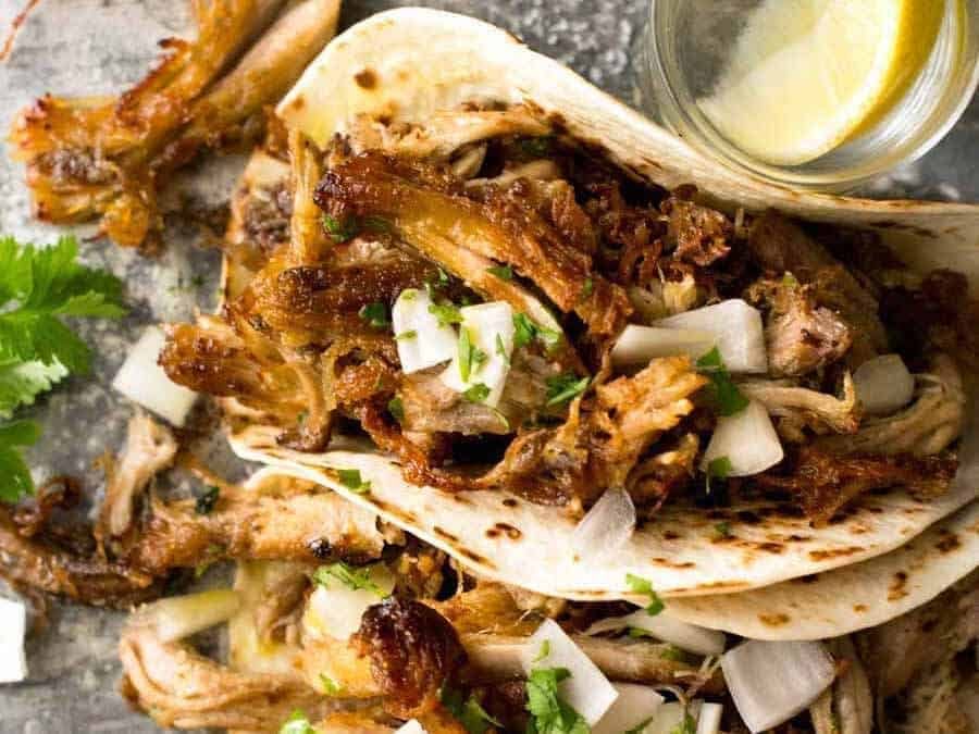 Overhead photo of two Pork Carnitas Tacos with tequila shots on the side.