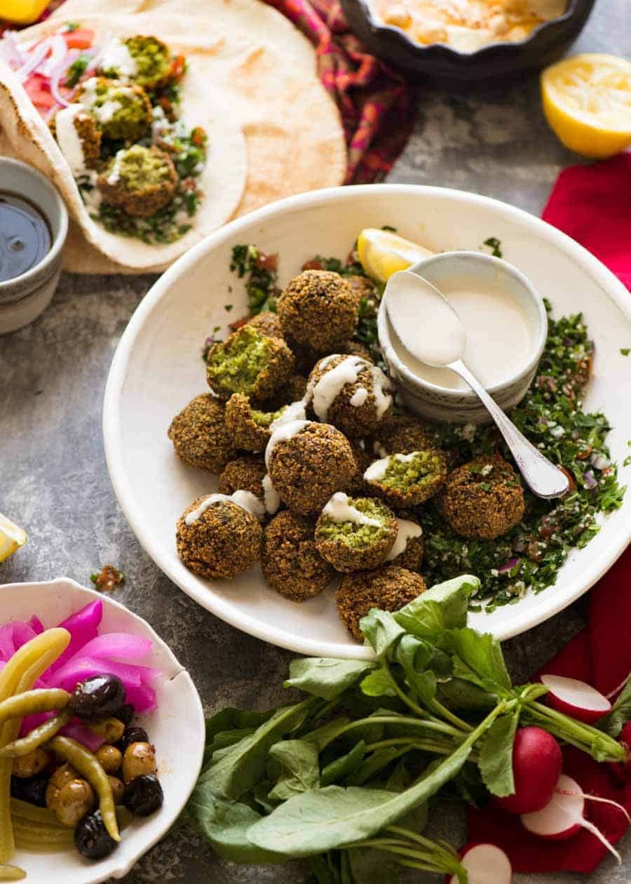 Falafels in a bowl with sides - tahini sauce, tabbouleh, hummus, pickles, wraps