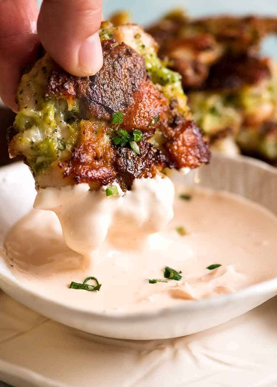 Hand dipping Broccoli Chicken Fritter into pink yogurt dipping sauce