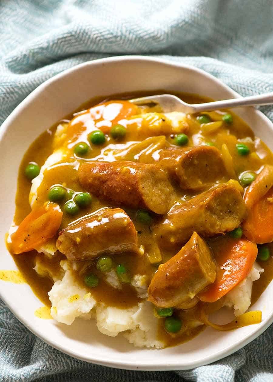 Curried Sausages in a white bowl served over mashed potatoes