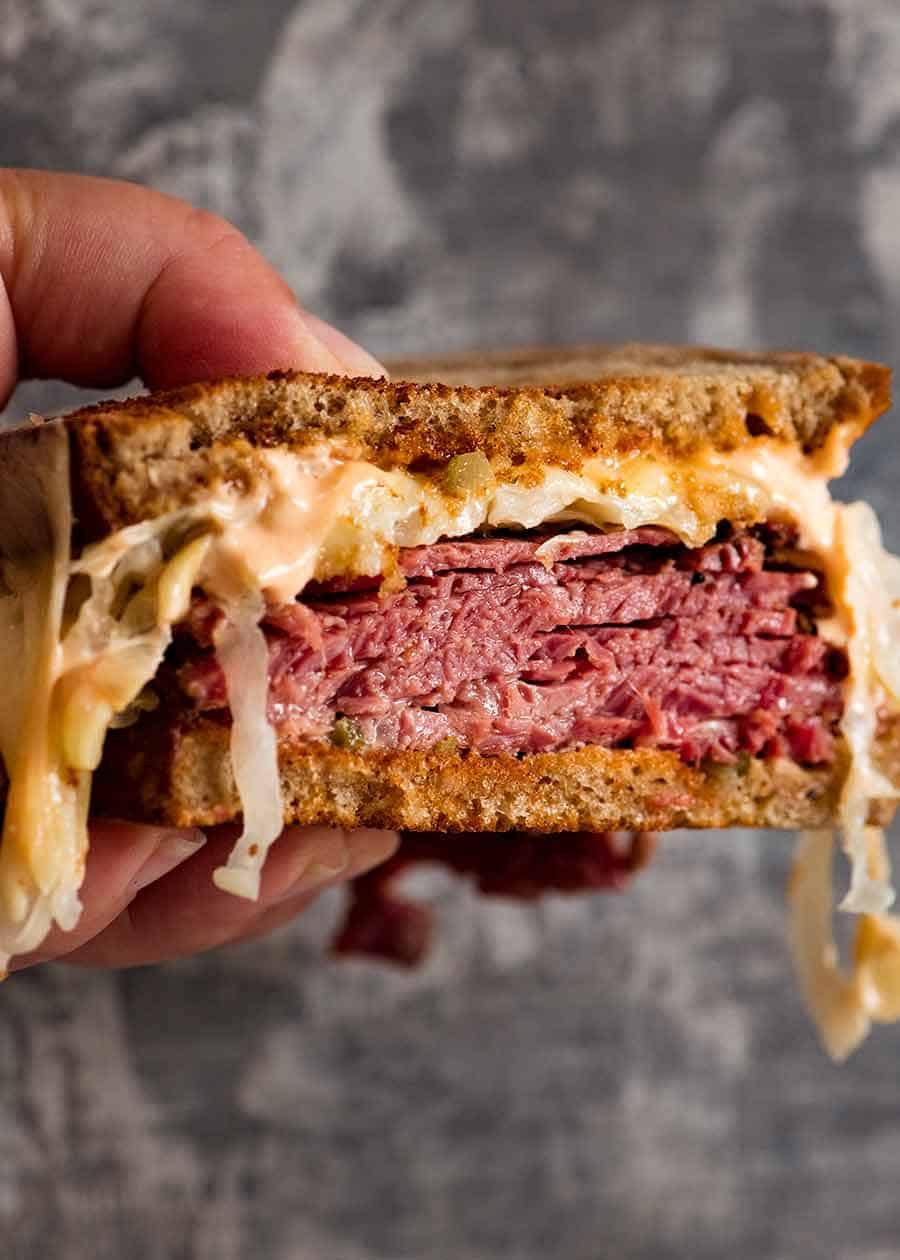 Reuben Sandwich loaded with homemade pastrami, easy quick sauerkraut, Russian Dressing, Swiss cheese on rye bread, ready to be eaten. Katz's deli copycat recipe.