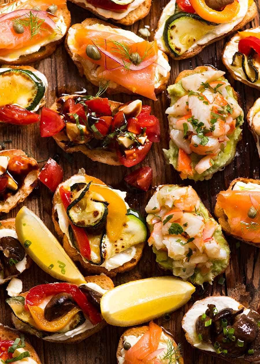 Wooden board filled with Crostini - Smoked Salmon, Shrimp Avocado, Mediterranean and Caprese