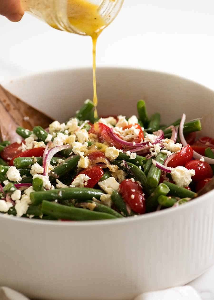 Drizzling lemon dressing over Green Bean Salad with Cherry Tomatoes and Feta