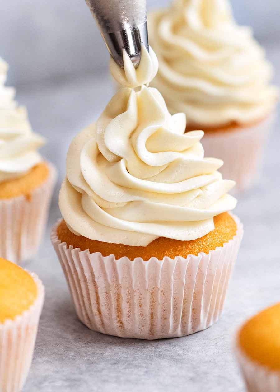 Close up piping Fluffy Vanilla Frosting onto Vanilla Cupcake