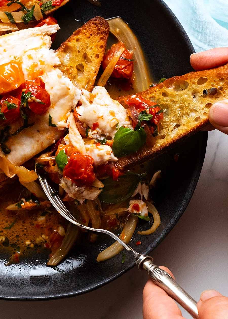 Fork piling Acqua Pazza Italian Poached Fish on a crispy garlic crostini